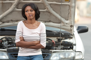 Frustrated woman sitting on hood of broken down car